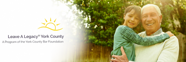 A smiling elderly man holds a young child in a sunny outdoor setting, with greenery in the background.