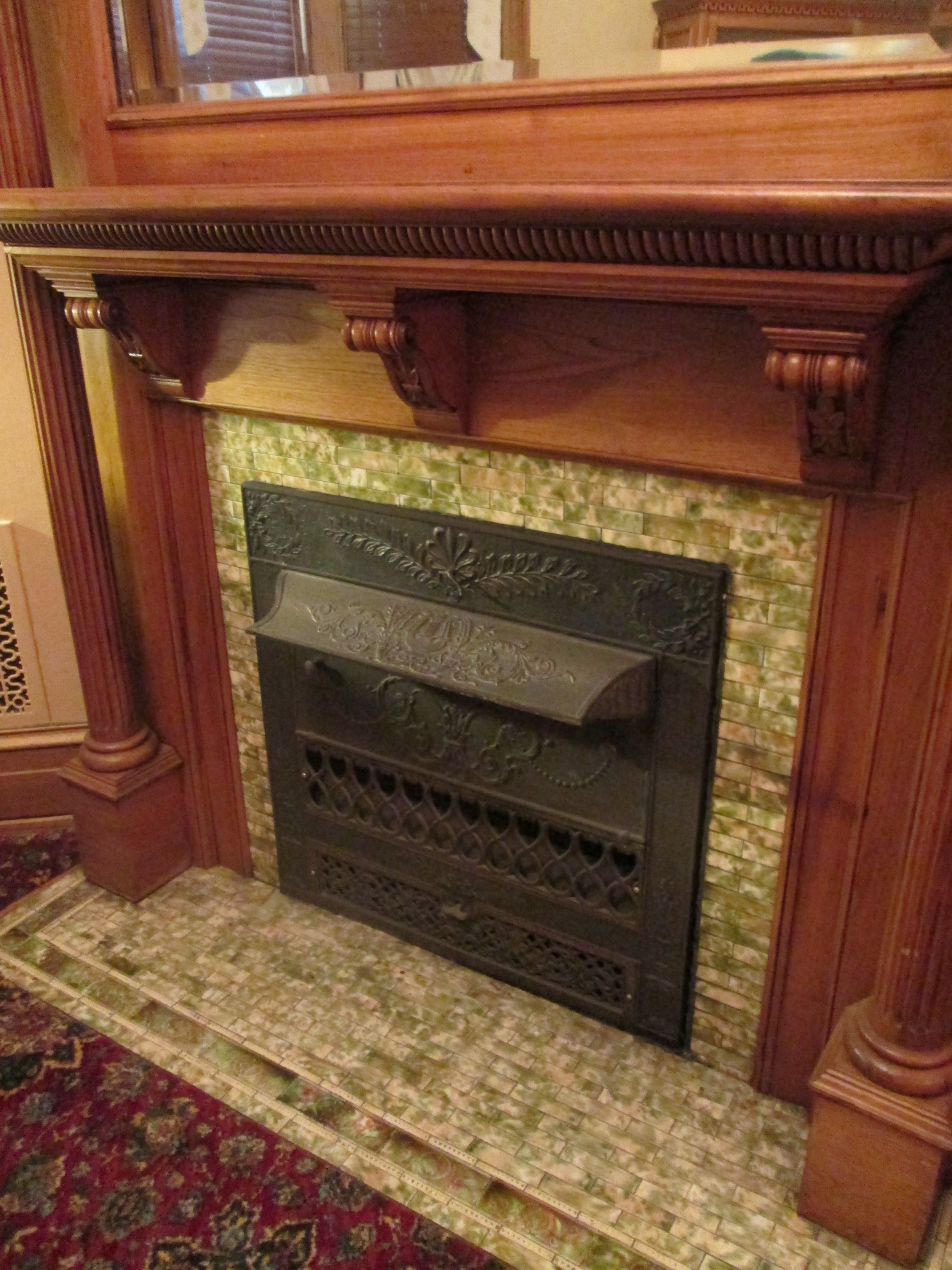 The fireplaces each have beautiful mantels with beveled mirrors and contain Victorian era cast iron grates and decorative glazed ceramic tile. The mottling of glazes was a very popular form of adding depth and decoration to the field tile used on hearths and facades from the 1900s to 1930s. However, the mantel woodworking is more along the neoclassical style with the use of elaborate carvings and Ionic columns.