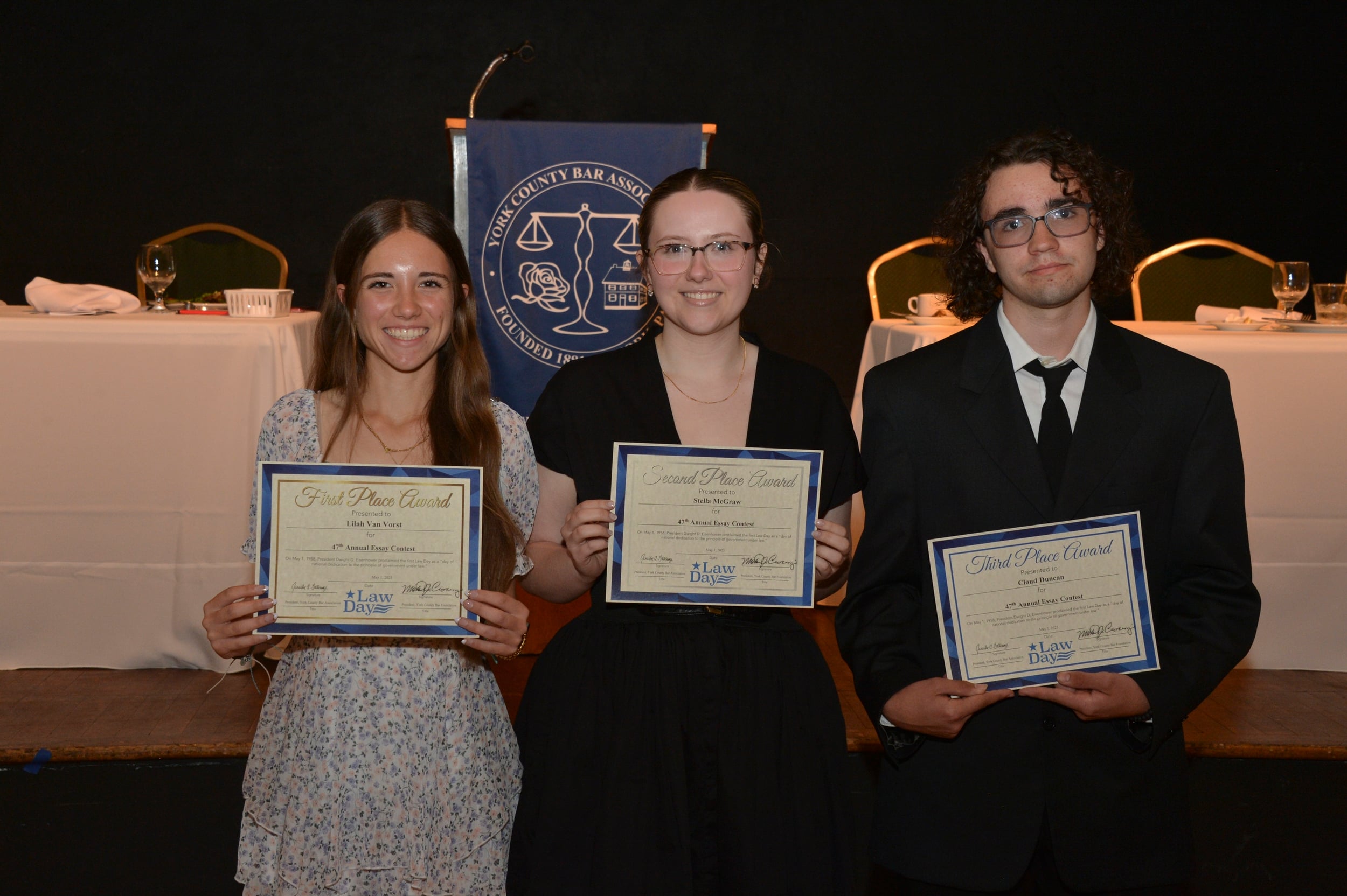 Three students hold their award certificates at a ceremony, with a backdrop featuring the York County Bar Association logo.