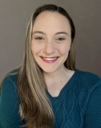 A smiling woman with long, straight hair wearing a teal sweater, set against a neutral background.